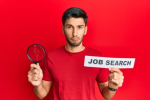 Young handsome man holding magnifying glass for job search depressed and worry for distress, crying angry and afraid. sad expression.
